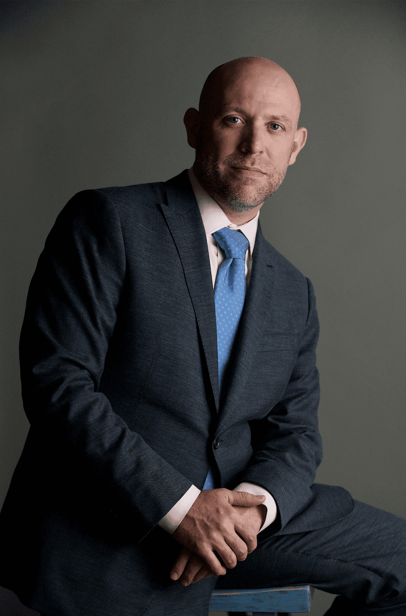 Screen Shot 2019-02-05 at 11.50.10 PM A man sitting on a stool in a suit and tie.